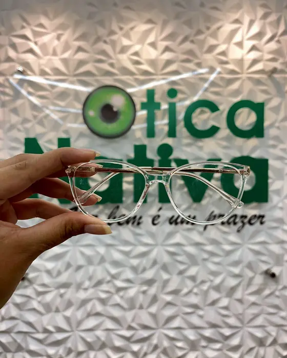 Mão segurando uma armação transparente diante da logo da Ótica Nativa
